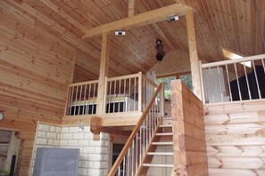 A wooden interior with a staircase, a hanging light fixture, and a brick fireplace. - Log cabin at the beginning (Thale-Friedrichsbrunn)
