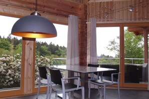 A wooden interior with a dining table and chairs, large windows, and a hanging light fixture. - Log cabin at the beginning (Thale-Friedrichsbrunn)