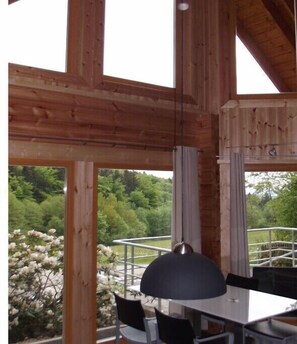 A wooden interior with large windows, a table, chairs, and a hanging pendant light. - Log cabin at the beginning (Thale-Friedrichsbrunn)