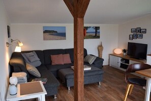 Ein Wohnzimmer mit Sofa, Hocker, TV-Schrank und Holzbalken.