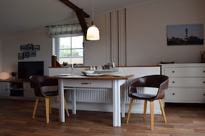 Ein Essbereich mit Tisch, Stühlen, einer Pendelleuchte, einem Fenster mit Jalousien, einer Heizung, einem Fernseher und einem Schrank.