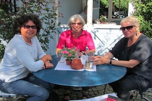 Drei Personen sitzen an einem Tisch im Freien, mit einem Blumentopf und Salzstreuern.