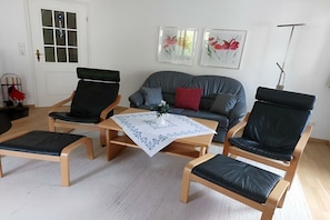 Ein Wohnzimmer mit einer Couch, zwei Sesseln, einem Couchtisch und einer Tür mit Fenster.