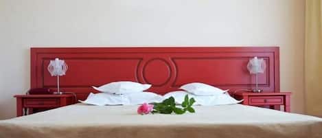 A neatly made bed with white linens, a pink rose, and two bedside lamps on matching red nightstands.