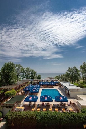 A pool area with umbrellas, lounge chairs, and a view of the sea.