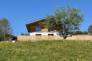 Ein modernes Holzhaus mit geneigtem Dach, einem Balkon und einem Baum davor.