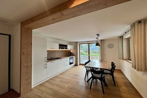 Eine moderne Küche mit weißen Schränken, ein Essbereich mit Tisch und Stühlen sowie ein großes Fenster mit Aussicht.