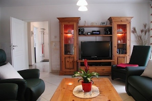 Ein Wohnzimmer mit Fernseher, Holzschränken, einem grünen Sofa und einem Couchtisch mit Pflanze.