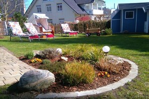 Ein Garten mit befestigtem Weg, Liegestühlen und einer kleinen Spielzone mit Ball und Spielzeugwagen.