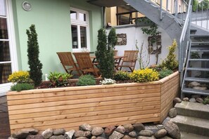 Ein Holz-Pflanzkasten mit Pflanzen, ein Holztisch mit Stühlen und eine Treppe.
