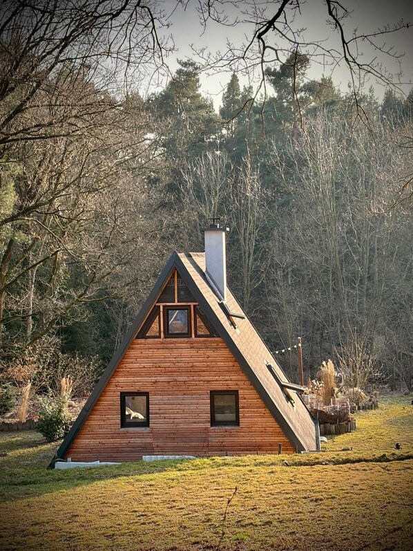 A wooden cabin with a triangular roof, a chimney, and two windows.