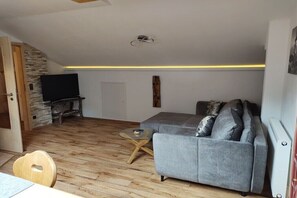 Ein Wohnzimmer mit grauem Sofa, Fernseher, Steinwand und Holzboden.