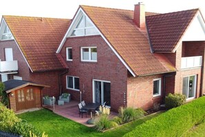 Ein zweistöckiges Haus mit Backsteinfassade, einem geneigten Dach und einer Terrasse mit Gartenmöbeln.