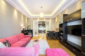 Ein modernes Wohnzimmer mit einem rosa Sofa, einem Fernseher und einem Essbereich.