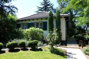 A house with a tiled roof, a front door, and a small garden with bushes and a pathway. - Holiday home with 1 bedroom (Bad Dürkheim)