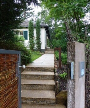 A set of stone steps leading to a house with a white exterior and green shutters, surrounded by lush greenery. - Holiday home with 1 bedroom (Bad Dürkheim)