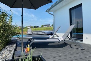 Eine Terrasse mit zwei Liegestühlen, einem Sonnenschirm und einem Grillbereich mit Flaschen.