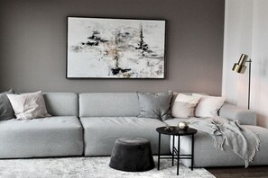 Ein modernes Wohnzimmer mit einem grauen Sofa, einem runden Hocker, einem kleinen Beistelltisch und einer Stehlampe.