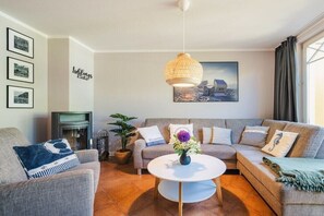 Ein Wohnzimmer mit einer Couch, einem Couchtisch, einer Pendelleuchte, einem Kamin und einem gerahmten Bild an der Wand.