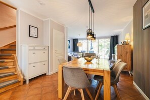 Ein Essbereich mit Holztisch, Stühlen, einer Chandelüster und einer Treppe.