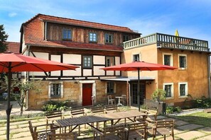A traditional building with a wooden facade, a balcony, and outdoor seating with red umbrellas. - Holiday home Lindenhof (Pirna)