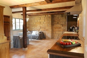 A rustic kitchen with exposed stone walls, wooden beams, and a breakfast bar with fruit. - Holiday home Lindenhof (Pirna)
