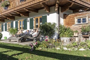 Ein traditionelles Chalet mit hölzernen Balkonen, einer Steinsitzbank und einem Garten mit verschiedenen Pflanzen.