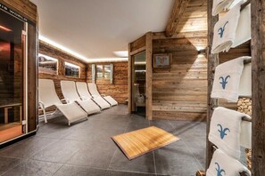 Ein Wellnessbereich mit Holzwänden, weißen Liegestühlen und einer Holzdusche.