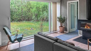 Een moderne woonkamer met een bank, een fauteuil, een open haard en een grote schuifglazen deur die uitkomt op een tuin.