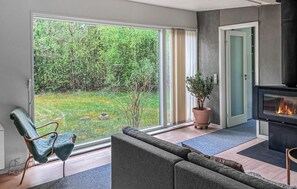 Ein modernes Wohnzimmer mit einer Couch, einem Sessel, einem Kamin und einer großen Schiebeglastür, die zu einem Garten führt.
