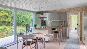 Een moderne keuken met grote ramen, een eethoek met een tafel en stoelen, en uitzicht op groen.