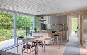 Eine moderne Küche mit großen Fenstern, einem Essbereich mit Tisch und Stühlen und Blick ins Grüne.