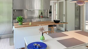 Een moderne keuken met een roestvrijstalen koelkast, een houten aanrecht en een eethoek met een witte tafel en blauw bord.