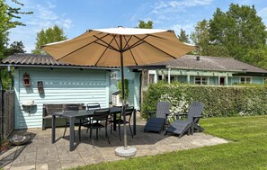 Eine Terrasse mit Tisch, Stühlen und einem großen Sonnenschirm, im Hintergrund ein Haus.