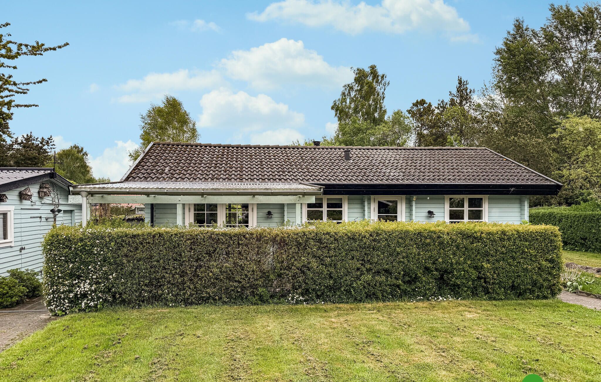 Een huis met twee verdiepingen, een pannendak, een overdekte veranda en een keurig onderhouden haag ervoor.