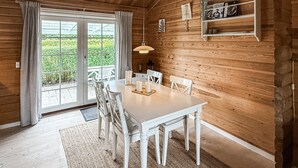 Un interior de madera con una mesa de comedor, sillas, una lámpara colgante y una ventana con cortinas.