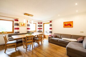 Ein Zimmer mit einem Holzesstisch, Stühlen, einer Couch und einem Fenster mit Vorhängen.