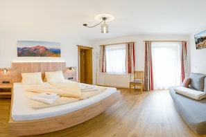Ein Schlafzimmer mit einem bogenförmigen Bett, einem Holzkopfende, einem Nachttisch, einem Sessel, einer Couch, einem Fenster mit Vorhängen und einer Wandleuchte.