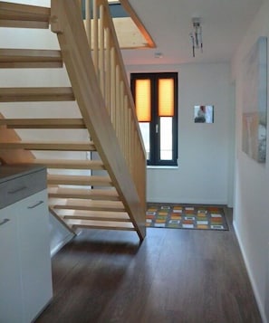 Eine Holztreppe führt zu einer Zwischenebene mit einem Fenster und einem kleinen Bildrahmen an der Wand.