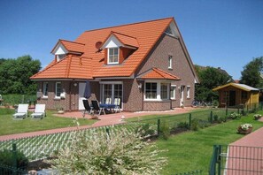 A two-story house with a red-tiled roof, a brick exterior, and a fenced backyard with a lawn and garden. - Holiday home with 2 bedrooms (Norddeich)