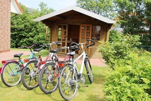 A wooden cabin with a porch, bicycles parked outside, and a brick building adjacent to it. - Holiday home with 2 bedrooms (Norddeich)
