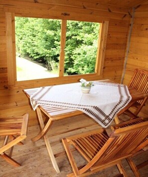 A wooden cabin interior with a table and chairs, a window with a view of greenery, and a small potted plant on the table. - Holiday home with 2 bedrooms (Norddeich)