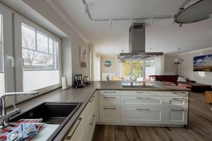 A modern kitchen with a central island, white cabinetry, and a large window providing natural light.
