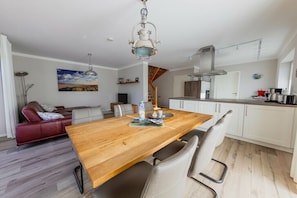 A modern kitchen with white cabinets, a wooden dining table, and a hanging light fixture.
