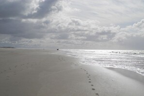 A beach with footprints leading to the water, a cloudy sky, and a distant shoreline. - Holiday apartment in Nebel with swimming pool (Nebel)