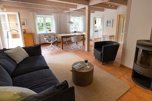 A living room with a sofa, a round coffee table, a fireplace, and a dining area with a table and chairs. - Holiday apartment in Nebel with swimming pool (Nebel)