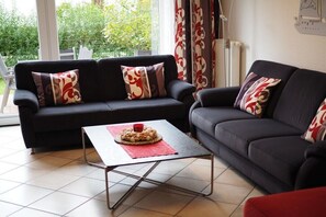 Ein Wohnzimmer mit zwei dunklen Sofas, einem Couchtisch und Blick auf Grünfläche.