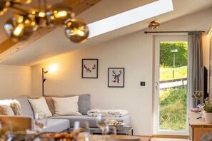 Ein gemütliches Wohnzimmer mit einer Couch, einem Esstisch mit Essen und einem großen Fenster mit Vorhängen.