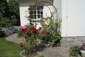 Ein Rosengarten, ein weißes Gebäude und eine Steinmauer.