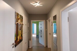 Ein Flur mit weißen Türen, einer Deckenleuchte und einem Gemälde an der linken Wand.
